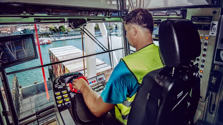Crane operator handling container cargo at a port terminal, showcasing precision and focus in operating advanced machinery for safe and efficient loading and unloading operations.