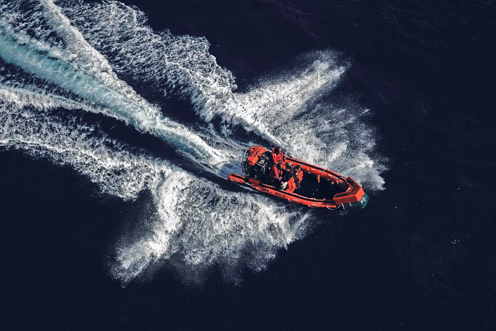 An aerial view of a rescue boat speeding through the water, creating waves as it cuts through the sea, highlighting rapid response capabilities and maritime safety operations.