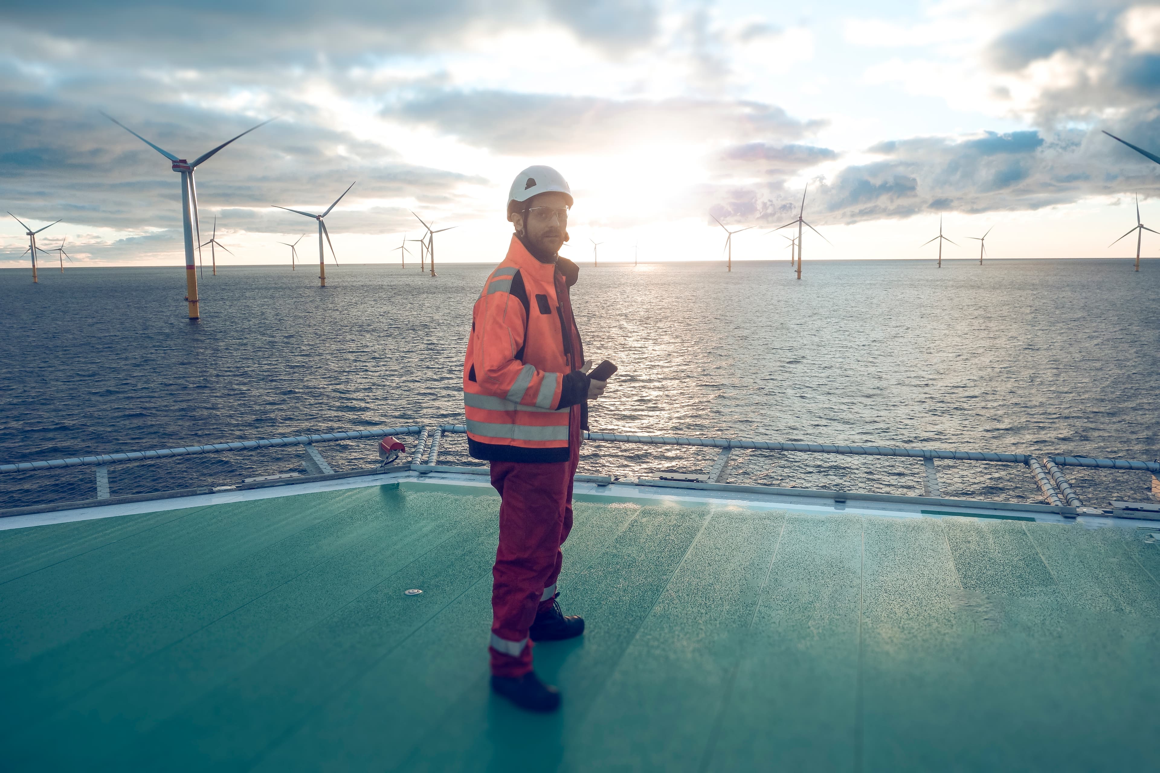 A man standing on a helipad offshore, overseeing operations and preparing for a helicopter landing amidst a dynamic marine environment.