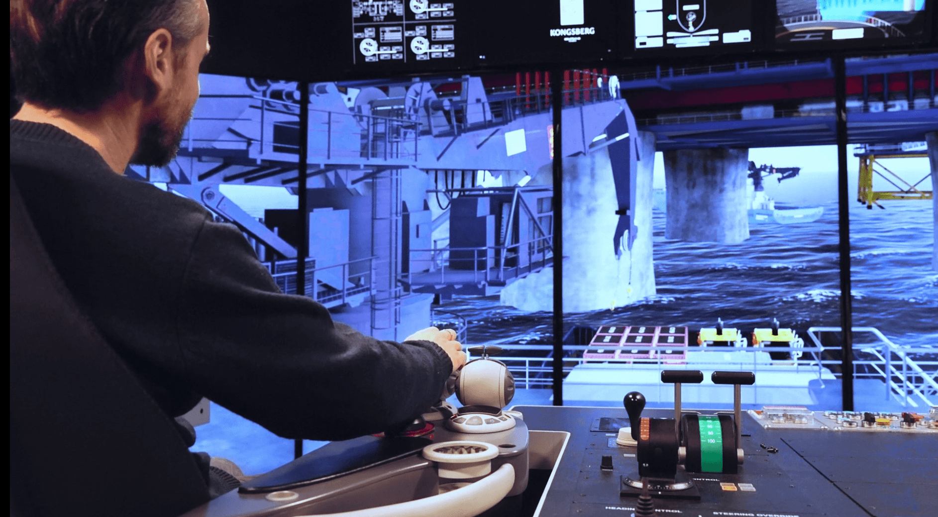 The image shows a person operating a maritime bridge simulator, with controls in front of them and a large screen displaying a simulated offshore environment. This setup is used for realistic training in marine operations.